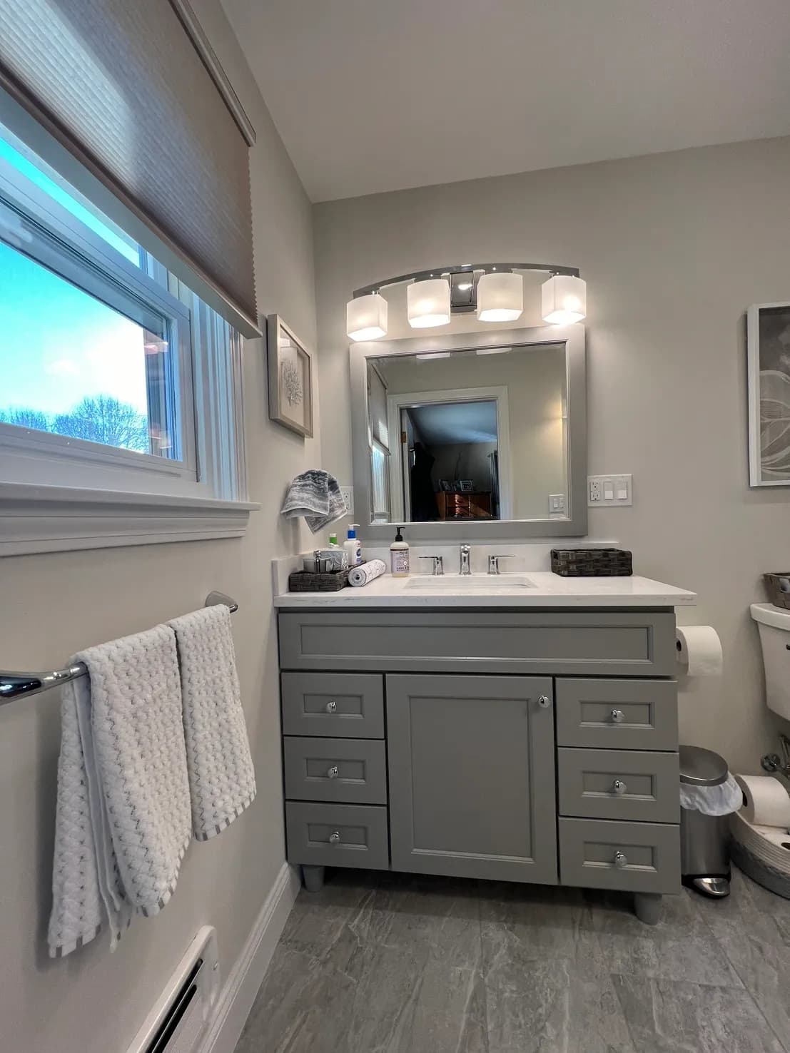 A finished bathroom remodel with a gray shaker vanity, quartz countertop, framed mirror, and tile floor