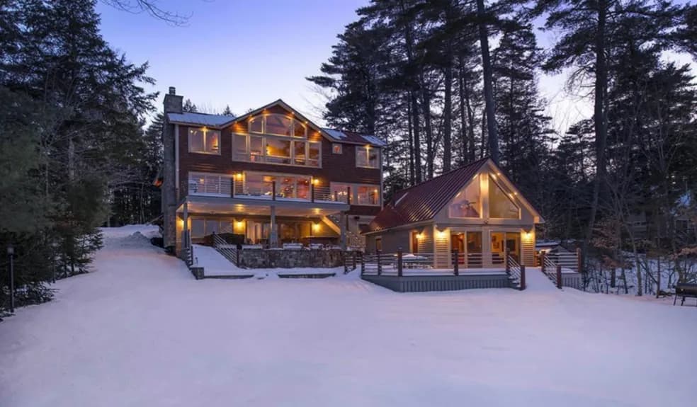 A completed multi-story custom lakefront home lit up at dusk in the snow, built by Adelphia Construction
