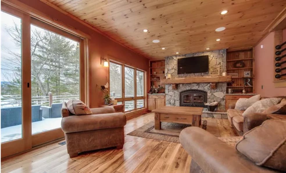 A finished living room with a floor-to-ceiling stone fireplace, pine cathedral ceiling, and hardwood floors