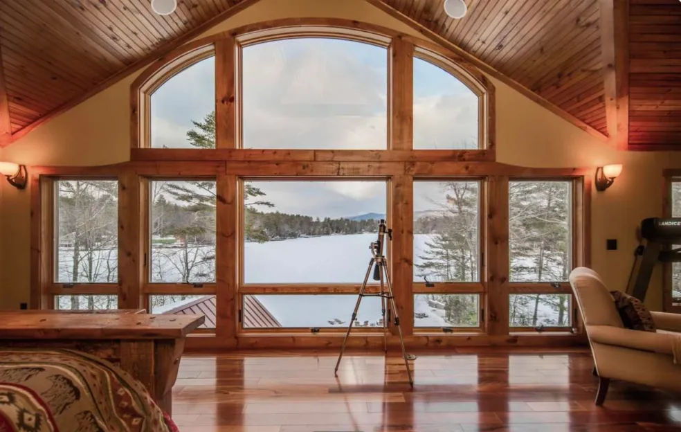 A finished custom room with an arched wood-framed window wall overlooking a lake and gleaming hardwood floors, built by Adelphia Construction